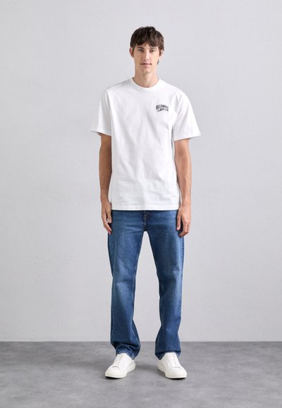 Tricou alb din bumbac, cu mâneci scurte, având un grafic mic de culoare neagră pe pieptul stâng. Combinat cu blugi din denim albastru și adidași albi.