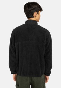 Pullover in pile nero con superficie testurizzata, colletto e vestibilità rilassata. Presenta un dettaglio di cucitura lungo la parte superiore della schiena.