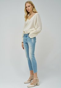Suéter de punto de color claro con escote en V, combinado con jeans de mezclilla clara desgastados. Zapatos de tacón bloque beige con correas de tobillo.