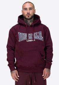 Bordowy hoodie wykonany z miękkiego materiału, z kieszenią z przodu, kapturem ze sznurkiem oraz odważnym logo "LONSDALE" w białym i niebieskim kolorze.