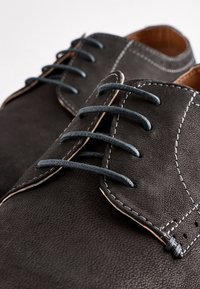 Black leather shoes with blue laces. Features contrasting white stitching and a textured finish. Design includes rounded toe and lace-up closure.