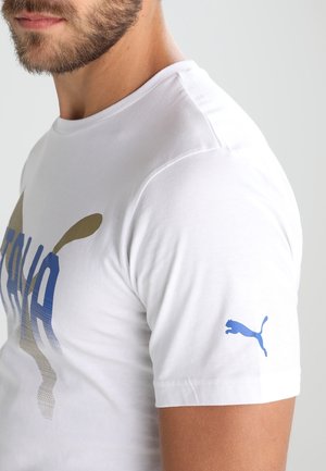T-shirt en coton blanc avec des graphiques bleus et dorés portant l'inscription "ITALIA." Logo Puma bleu sur la manche gauche. Design à manches courtes et col rond.