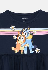 Μπλουζάκι στρατιωτικού χρώματος με γραφικό δύο καρτούν σκύλων, με φρουφρουτίστερη τulle στρώση στο κάτω μέρος και πολύχρωμες ριγέ λεπτομέρειες και μαργαρίτες.