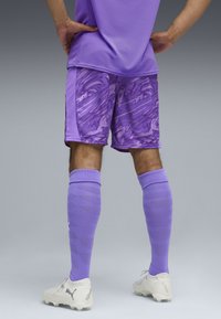 Pantaloni corti da allenamento viola con un motivo marmorizzato, abbinati a calze viola coordinate. Indossati con scarpe da calcio bianche con dettagli testurizzati.