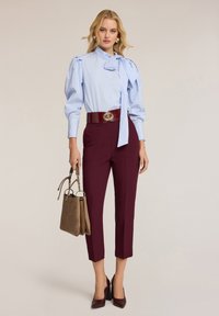 Helles blau gestreiftes Blusenshirt mit Schleifendetail, bordeauxfarbene, hochgeschnittene, maßgeschneiderte Hose und braune Handtasche kombiniert mit bordeauxfarbenen High Heels.