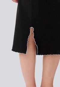 Jupe noire à côtes avec un ourlet festonné blanc et une fente frontale à bord ondulé, mettant en valeur la texture et les détails de design uniques.