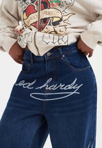 Tummansiniset farkut, joissa on kevyt haalistu. Edessä on suuri valkoinen logo, viisi taskua ja klassinen suora lahje.