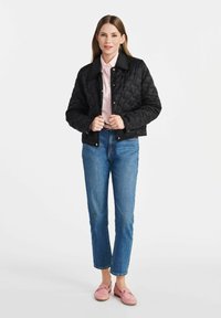 Czarna pikowana kurtka z zatrzaskami, noszona na jasnoróżowej koszuli w paski, zestawiona z niebieskimi dżinsami i różowymi loafersami. Gładkie tekstury, krótki fason.