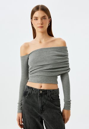 Grijze off-shoulder top met lange mouwen, met verzamelde stof, geribbelde textuur en een cropped ontwerp, gecombineerd met donkere denim jeans.