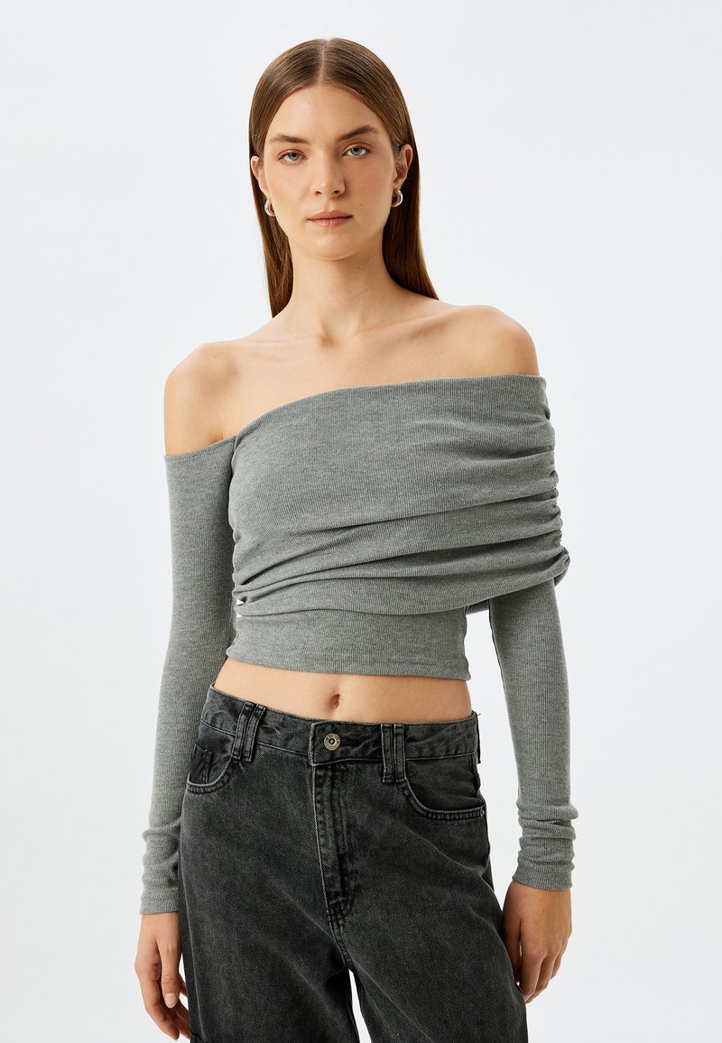 Grauer schulterfreier Langarmtop mit gerafftem Stoff, gerippter Textur und cropped Design, kombiniert mit dunklen Denim-Jeans.