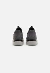 Zapatillas deportivas de malla en gris oscuro con una parte superior texturizada, acentos negros y una suela blanca flexible. Presenta una lengüeta en el talón.