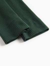 Tecidos canelados de cor verde-escuro dobrados com costura visível sobre um fundo claro.