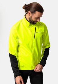 Fosforyzująca żółta kurtka typu softshell z czarnymi rękawami, zapięciem na zamek błyskawiczny na piersi, odblaskowymi detalami oraz gładkim, teksturowanym wykończeniem.
