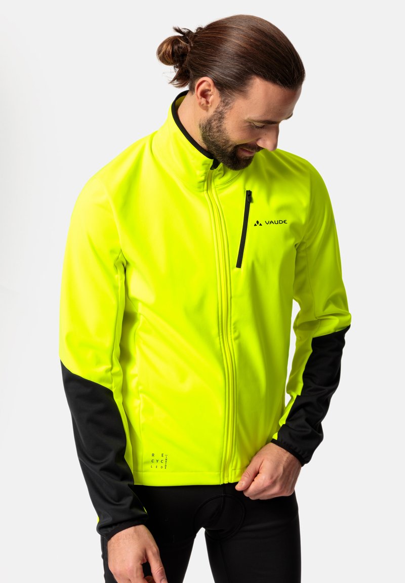 Fosforyzująca żółta kurtka typu softshell z czarnymi rękawami, zapięciem na zamek błyskawiczny na piersi, odblaskowymi detalami oraz gładkim, teksturowanym wykończeniem.