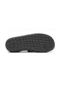 Suela de zapato de goma negra con patrón de agarre texturizado y secciones elevadas para tracción, con un diseño de logo circular cerca del talón.