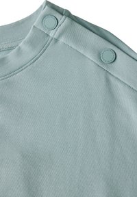 Camicia azzurra in cotone a maniche corte con colletto arrotondato, tessuto testurizzato e due bottoni a pressione sulla spalla sinistra.