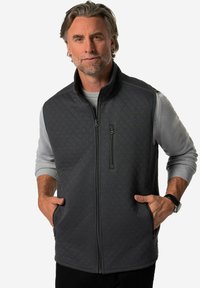 Grå vadderad väst med hög krage, framficka med dragkedja och sidofickor. Mjuk tyg med matt yta. Bärs över en ljusgrå tröja.