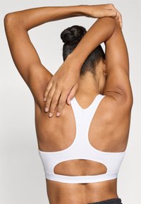 Λευκό αθλητικό σουτιέν με σχέδιο racerback και διακοσμητικές ανοίγματα. Ομαλό υλικό και εφαρμοστή γραμμή που αναδεικνύει την πλάτη.