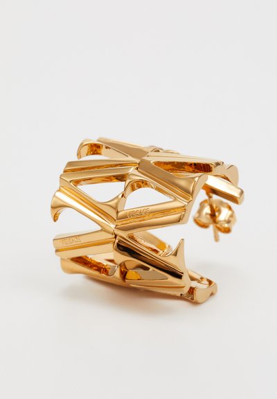 Bracelet de poignets doré avec un design géométrique entrelacé, présentant des surfaces lisses et des détails découpés pour une apparence audacieuse et moderne.