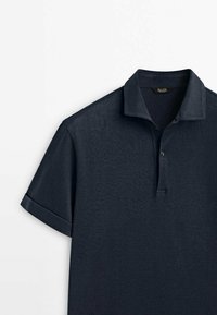 Polo bleu marine en tissu doux, doté d'un col à revers, d'une patte à deux boutons et de manches courtes retroussées. Texture lisse.
