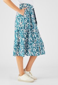 Jupe midi fleurie avec un motif turquoise et blanc, dotée d'une taille haute, de poches latérales et d'une fente au bas. Associée à des baskets blanches.