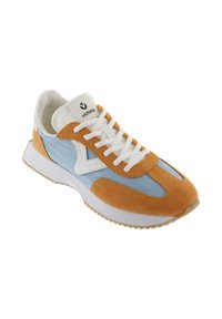 Baskets basses en tissu bleu clair, avec des empiècements en daim beige, des lacets blancs et une semelle blanche, arborant un logo "victoria" sur la languette.