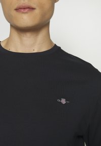 Camiseta de algodón azul marino con cuello redondo y mangas cortas, con un pequeño logo bordado en el pecho. Textura suave.