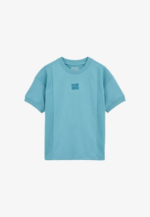 T-shirt bleu, à manches courtes, en tissu doux, avec un logo texturé au centre. Encolure arrondie et coupe décontractée.