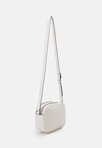 Bílá kožená crossbody taška obdélníkového tvaru, s hladkým povrchem, nastavitelným popruhem a jemnými černými akcenty po obvodu.