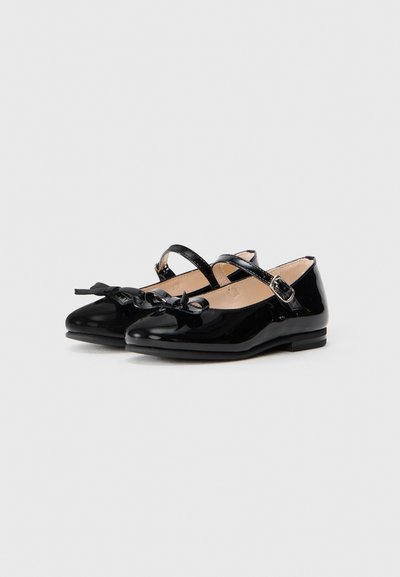 Bottines Mary Jane en cuir verni noir avec un bout arrondi, une sangle ajustable et un nœud décoratif à l'avant. Semelle plate, texture lisse.