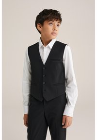 Černá vesta se třemi knoflíky, dvěma předními kapsami a klopou s výřezem, nošená přes bílou košili; střih na míru, hladká textura.