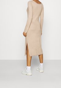 Robe beige en maille à manches longues avec une fente haute sur le côté gauche, associée à des baskets claires et des chaussettes blanches aux chevilles. Texture douce, coupe moulante.