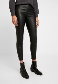 Svarta leggings i konstläder med en smal passform, medelhög midja och ankellångt snitt, matchade med svarta texturerade ankelstövlar.