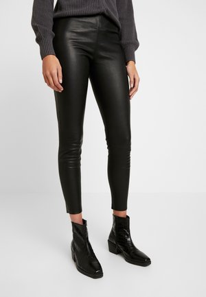Leggings en simili cuir noirs avec une coupe slim, taille mi-haute et longueur cheville, associés à des bottines noires texturées.