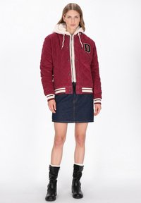 Bordowa bomberka sztruksowa z białą sztuczną podszewką futrzaną, mankietami w paski i zapinana na zatrzaski, noszona na dżinsowej spódnicy i czarnych butach.