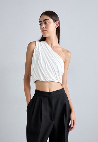 Haut blanc à épaules dénudées avec un tissu drapé, taille froncée, associé à un pantalon noir taille haute avec des plis à l'avant.