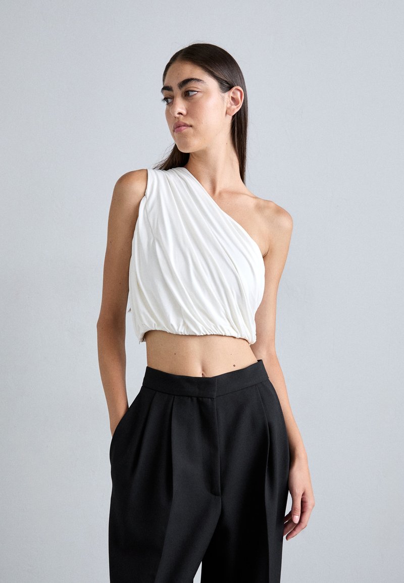 Hvit off-shoulder topp med drapert stoff, samla midje, kombinert med svarte høytlivs bukser med frontfeller.