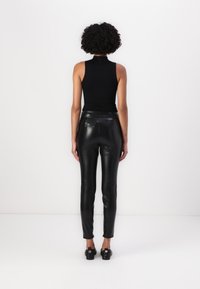 Čierny bezrukávový top v kombinácii s vysokými čiernymi nohavicami z umelej kože. Tento outfit sa vyznačuje priliehavým strihom a hladkou textúrou.