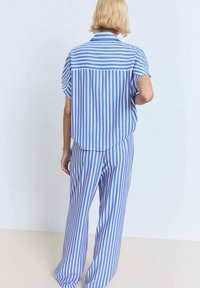 Chemise à manches courtes rayée bleuie avec un pantalon long assorti, présentant des rayures horizontales et verticales en bleu et rose clair. Texture de tissu lisse.