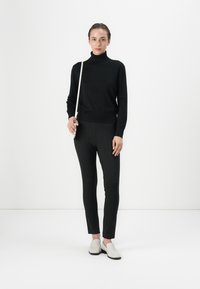 Black turtleneck sweater, fitted black pants, and light gray slip-on shoes. Minimalist design with a smooth texture and simple accents.