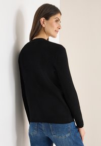 Czarny prążkowany sweter z długimi rękawami, okrągłym dekoltem i luźnym krojem, zestawiony z niebieskimi dżinsami. Materiał jest miękki i elastyczny.