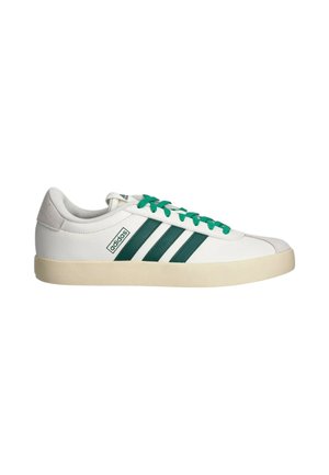 Sneaker Adidas bassa bianca con strisce e lacci verdi, suola beige e linguetta in suede sul tallone, su sfondo bianco.