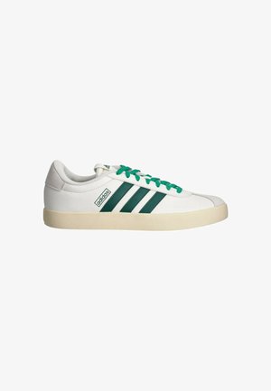 Weißer Low-Top Adidas Sneaker mit grünen Streifen und Schnürsenkeln, beigem Sohlen und Wildleder-Fersenlasche auf weißem Hintergrund.
