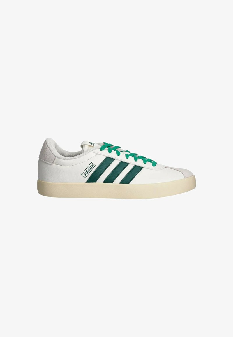 Sneaker Adidas bassa bianca con strisce e lacci verdi, suola beige e linguetta in suede sul tallone, su sfondo bianco.