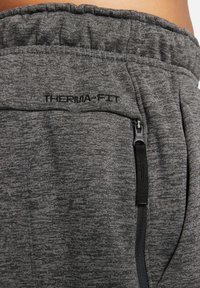 Gros plan sur un pantalon en tissu thermique gris moulant avec une ceinture élastique et une poche zippée dotée d'une languette noire et de détails de couture.