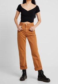 Sort kortærmet slå-om-top kombineret med højtaljede, opkrogede beige bukser og sorte snøreløse militærstøvler med tykke såler.