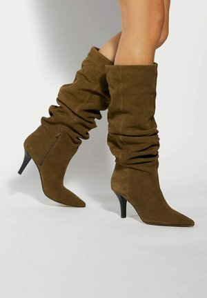Olive green suede over-the-knee boots with a slouchy design, pointed toe, and a black stiletto heel; features a side zipper for easy wear.
