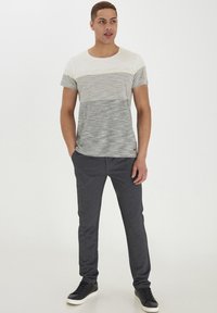 Grå og hvidstribet t-shirt med round neck, grå sweatpants og sorte sneakers, stående foran en neutral baggrund.