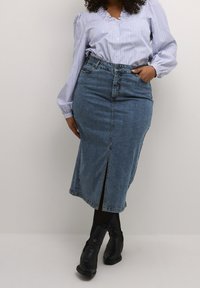 Falda lápiz de mezclilla con una abertura en la parte delantera central, lavado medio, diseño de cintura alta, combinada con una blusa a rayas y botas negras hasta la rodilla.