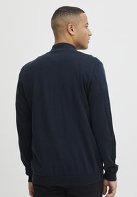 Mørkeblå langermet cardigan laget av mykt strikket stoff, med en ribbestrikket krage og mansjetter, samt en ensfarget strukturert bakdesign.